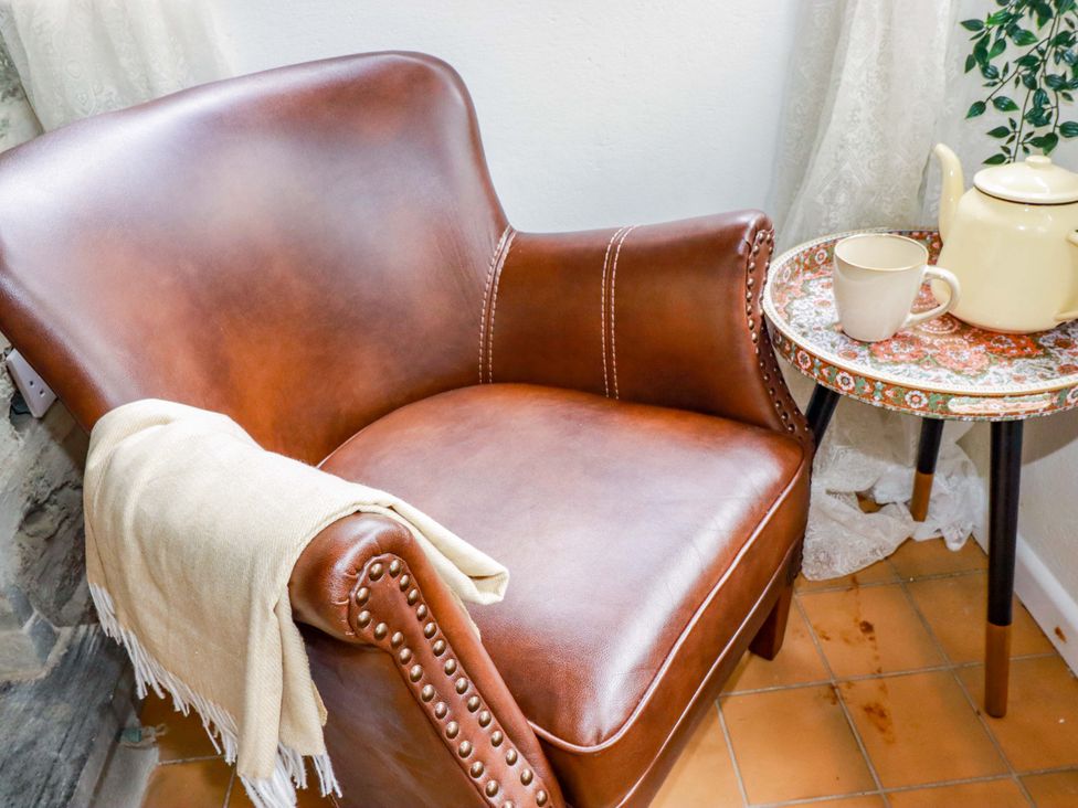 A snug with an armchair and a table with a cup and teapot at Sunnybrae Cottage in Tintagel