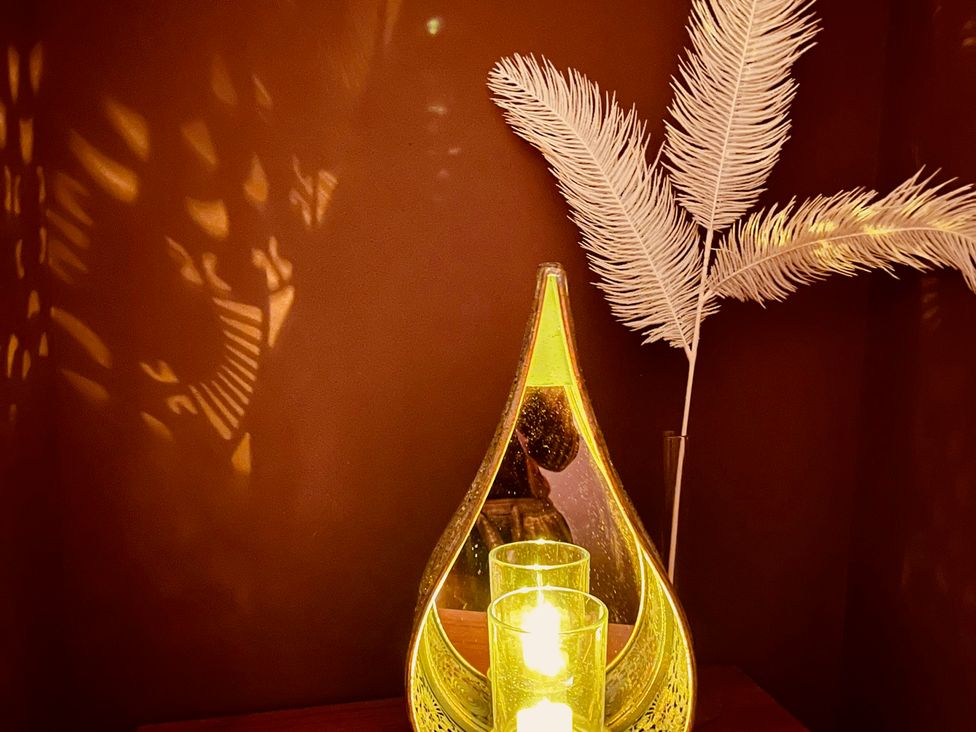 A lamp and candles on a table with a feather vase at Sunnybrae Cottage, Tintagel