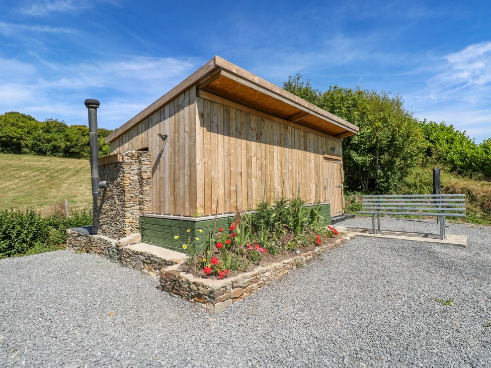 A wooden building with a stone wall and bench in an outdoor area at Thelma’s Lodge near Pontyates