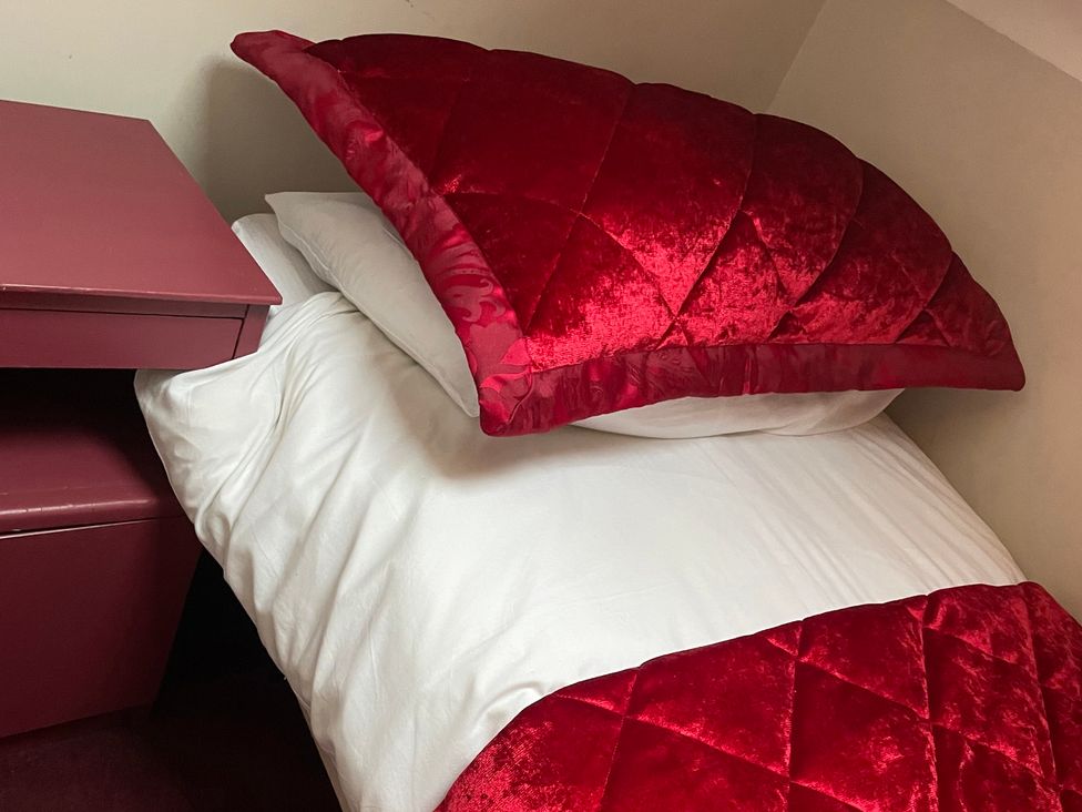 A bed with red bedding and a nightstand at The Bittern, Blakeney, Norfolk
