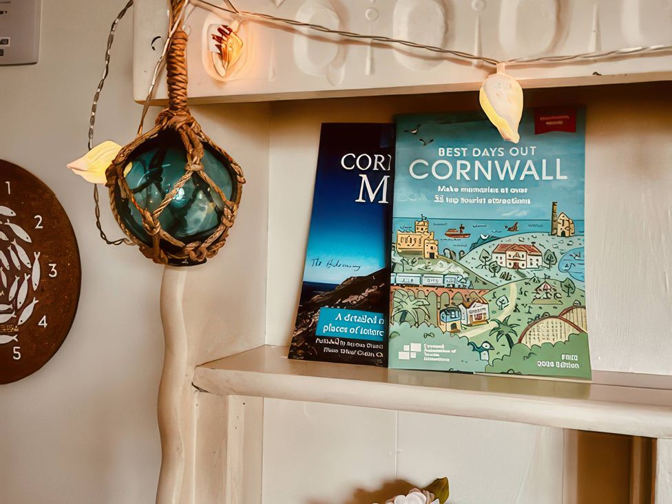 A shelf with guidebooks and a fishing float in a living room at The Hideaway in Tintagel