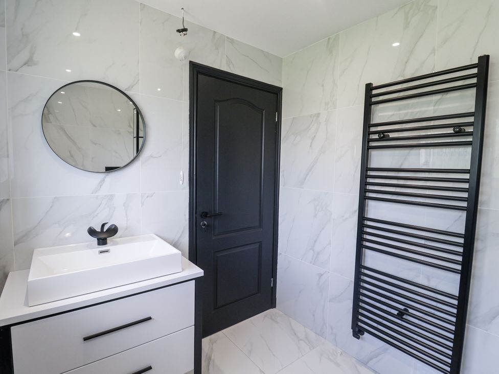 A bathroom with a sink, mirror, and towel warmer at Holly Farm in Colchester
