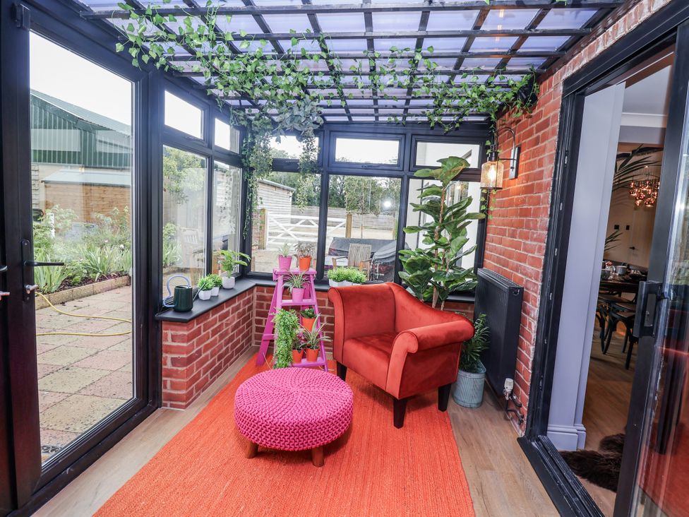 A conservatory with a red chair and plants at Holly Farm in Brantham