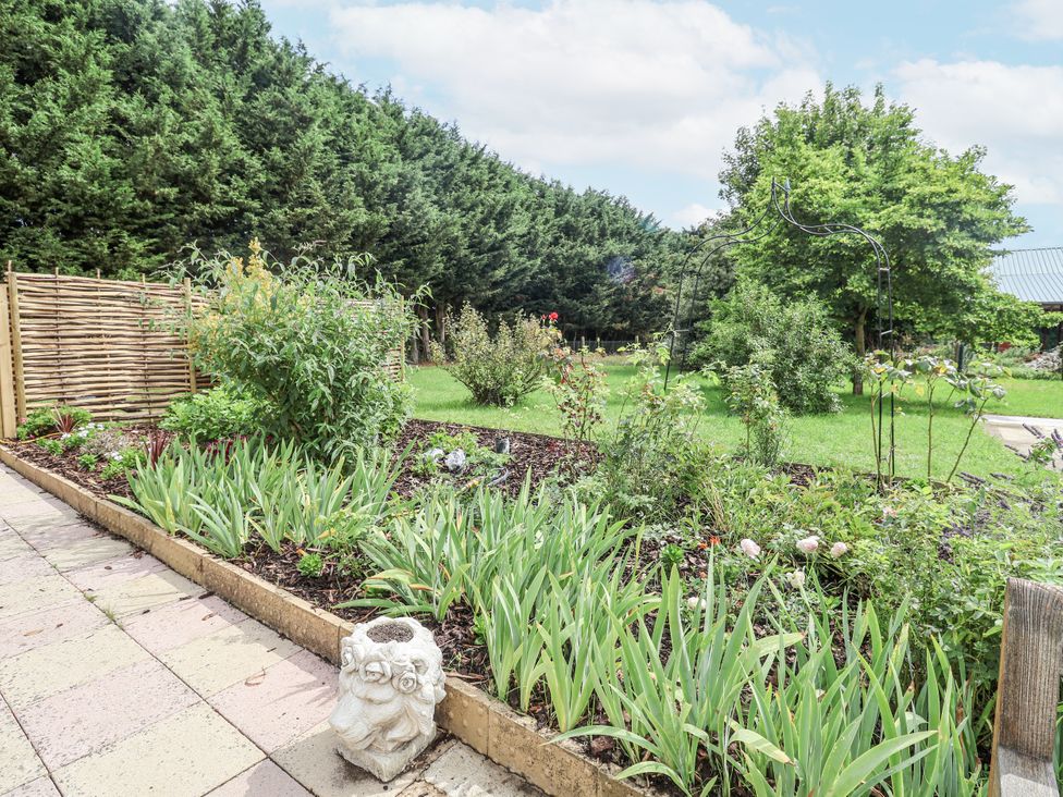 A garden with flower beds and a patio at Holly Farm in Brantham