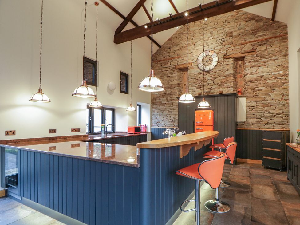 A kitchen with a stone wall and bar stools at The Barn at Sunny Barn in Brecon
