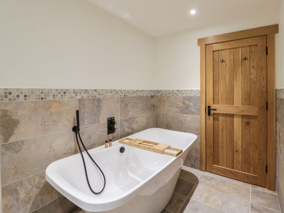 A bathroom with a bathtub and wooden door at The Barn at Sunny Barn in Brecon