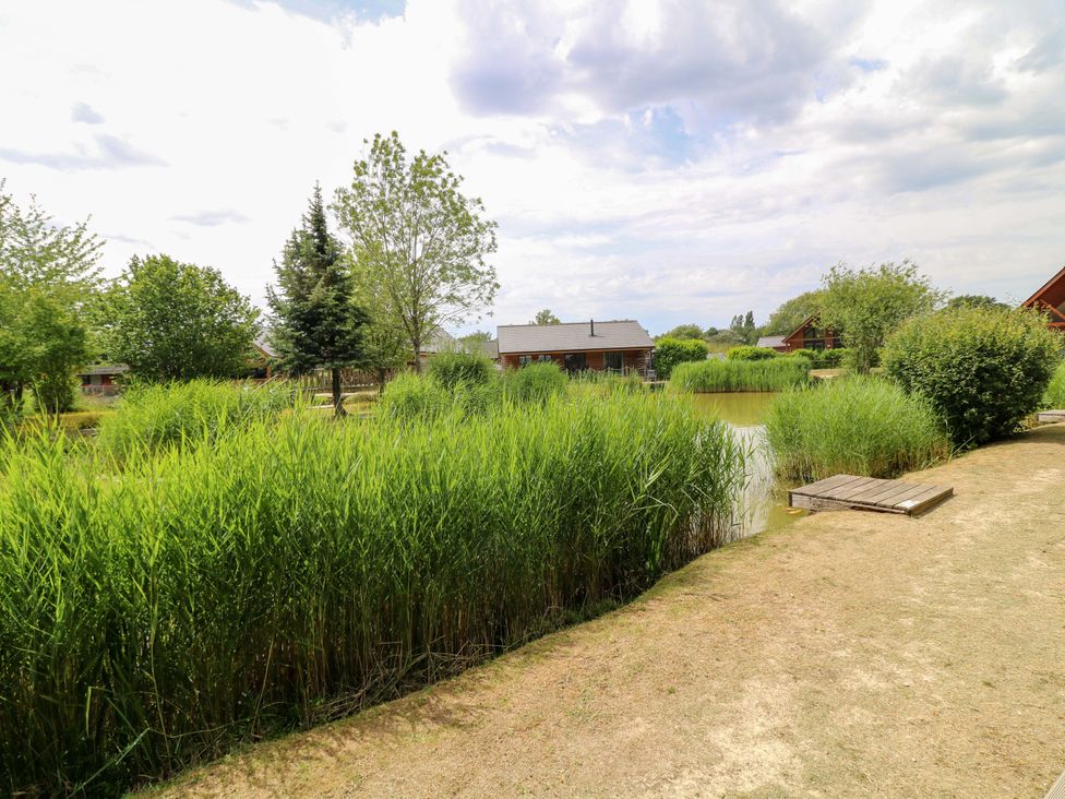 A pond surrounded by grass and trees with cabins at Sunnyside Lodge Thorpe-On-The-Hill