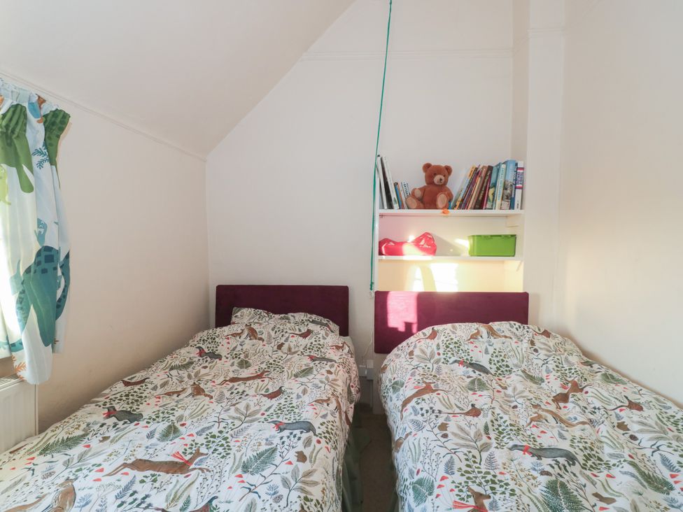A bedroom with two beds and a shelf with books at Vine Cottage in Alderton