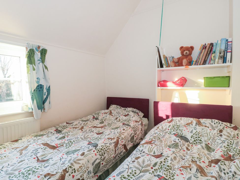 A bedroom with two beds and a shelf containing books at Vine Cottage in Alderton