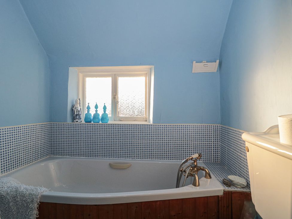 A bathroom with a bathtub and window at Vine Cottage in Alderton