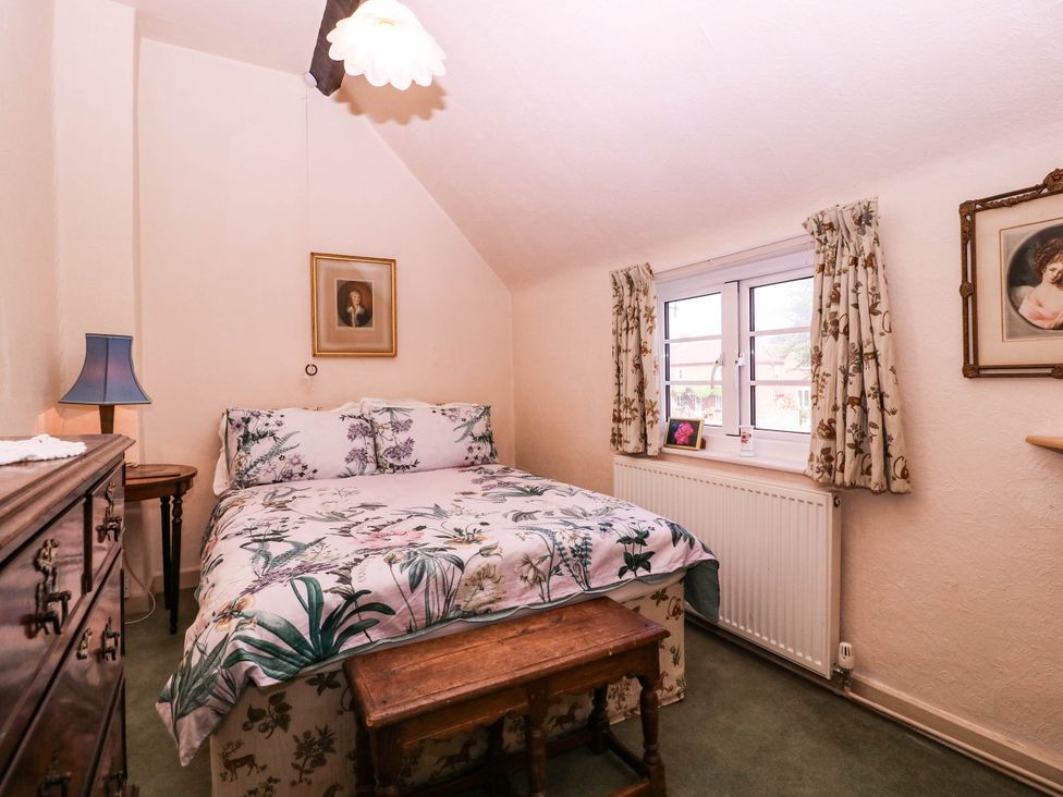 A bedroom with a bed, nightstand, and paintings at Vine Cottage in Cheltenham