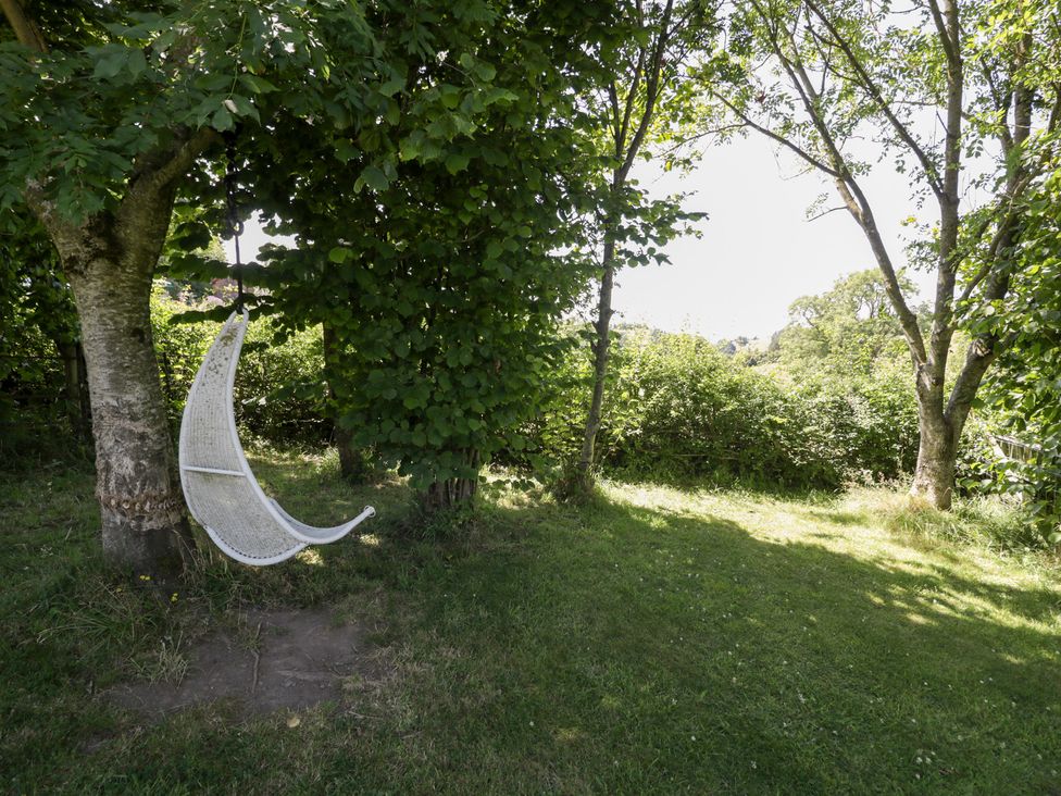 A garden with a hanging white hammock among trees at Owl Cottage in Llangollen
