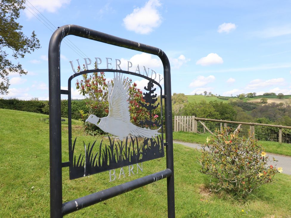 A sign for Upper Pandy Barn with grass and trees in the background at Upper Pandy Farm near Berriew