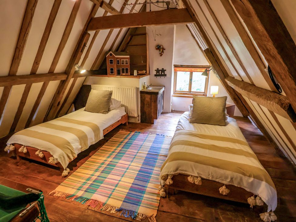 A bedroom with two beds, a table, and a window at Keirs Cottage in Carlton Colville
