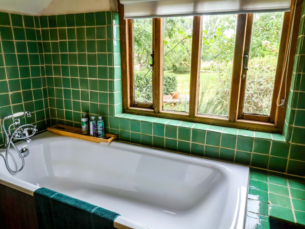 A bathroom with a bathtub and window overlooking a garden at Keirs Cottage in Carlton Colville