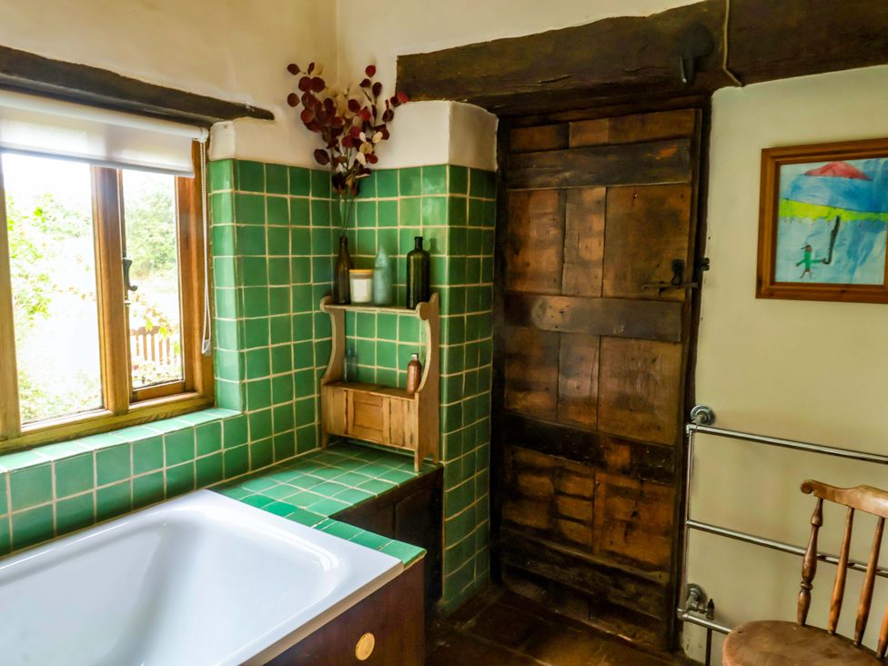 A bathroom with a bath tub and green tiled walls at Keirs Cottage in Carlton Colville