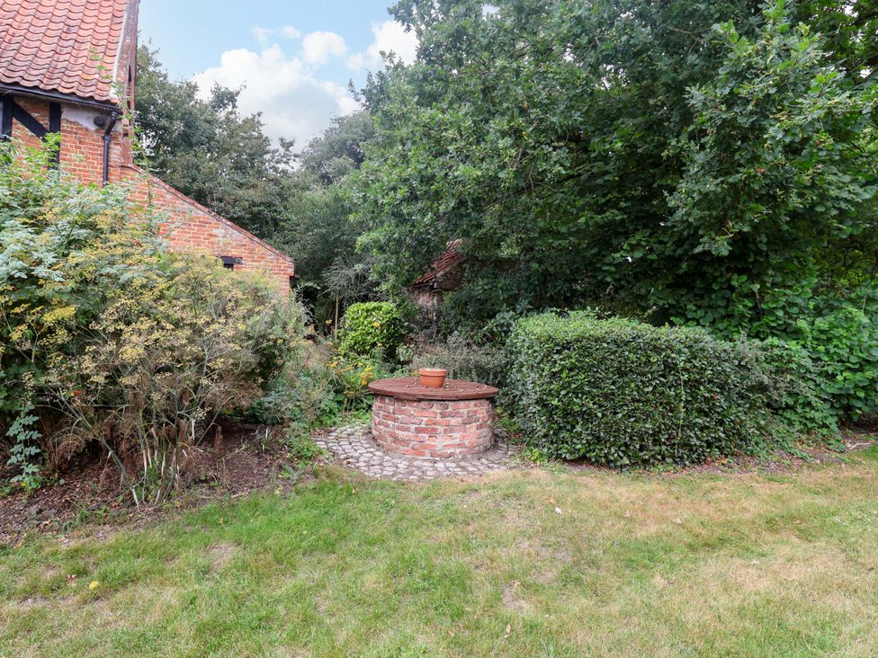 A garden with a brick well and flower pot at Keirs Cottage in Carlton Colville