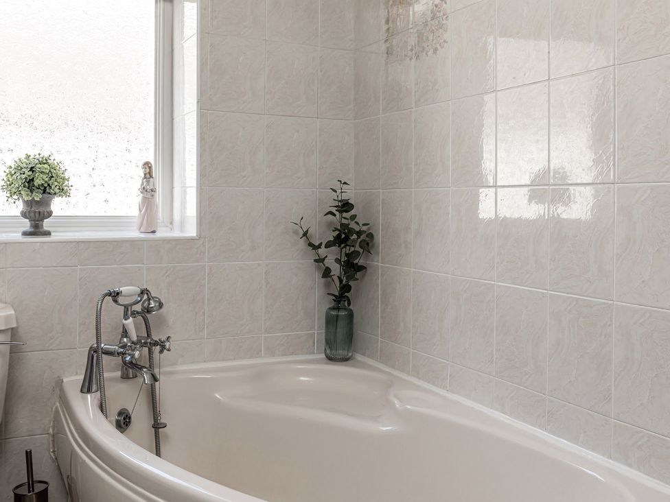 A bathroom with a bathtub and a plant on the window sill at The Crows Nest in Buxton