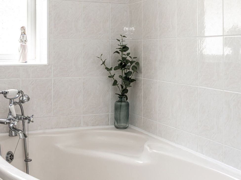 A bathroom with a bathtub and a plant in a glass vase at The Crows Nest in Buxton