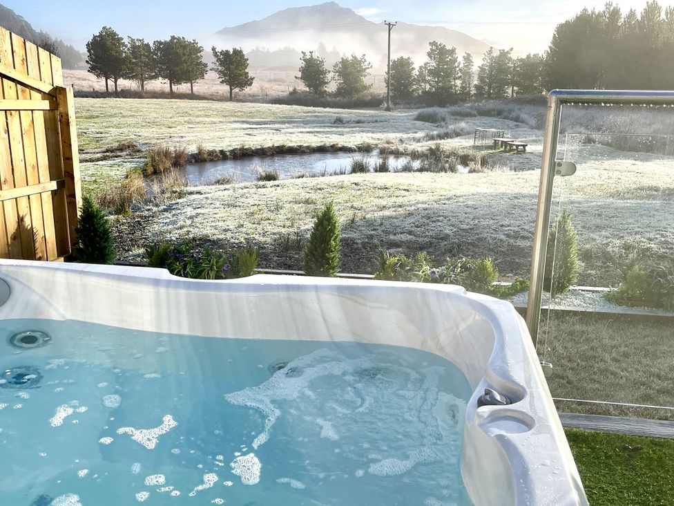 A hot tub with water overlooking a field and mountains at Crofters Suite