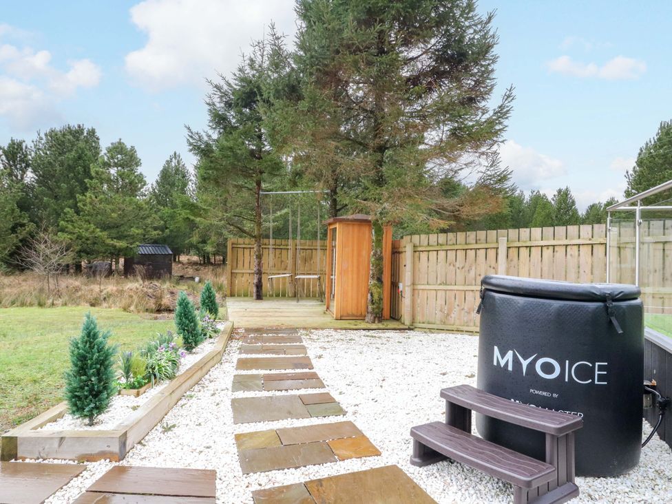 An outdoor area with a spa, tree, and stone path at Crofters Suite