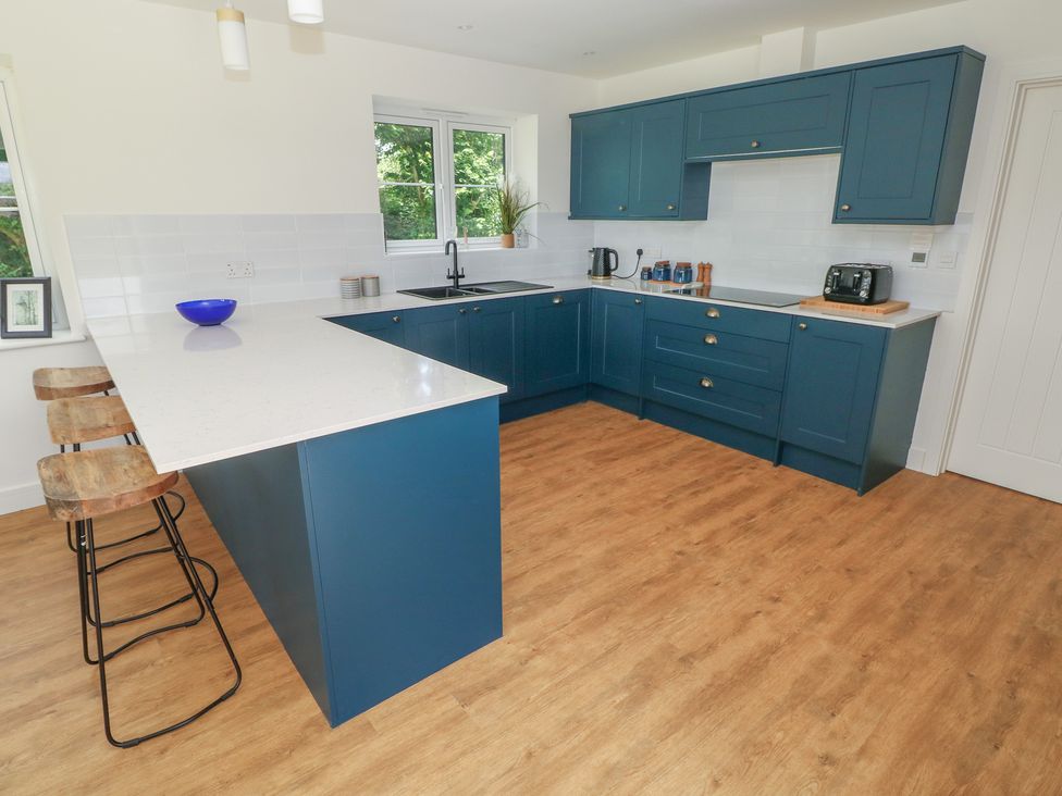 A kitchen with blue cabinets and bar stools at Ty Landsker in Milford Haven
