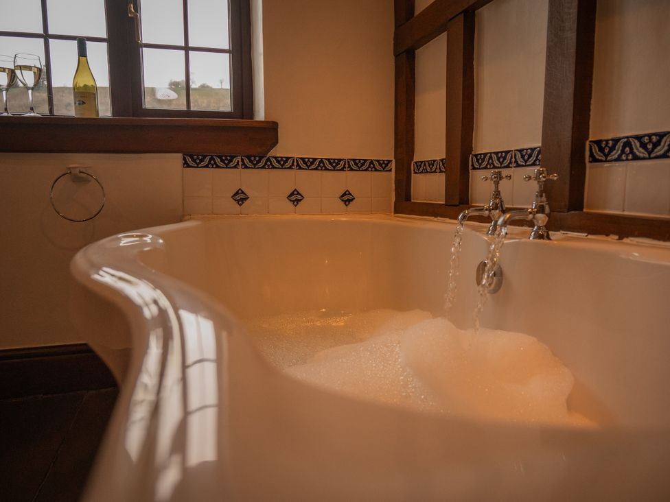 A bathtub with bubbles and a wine bottle at Stud Farm House Bleddfa near Knighton