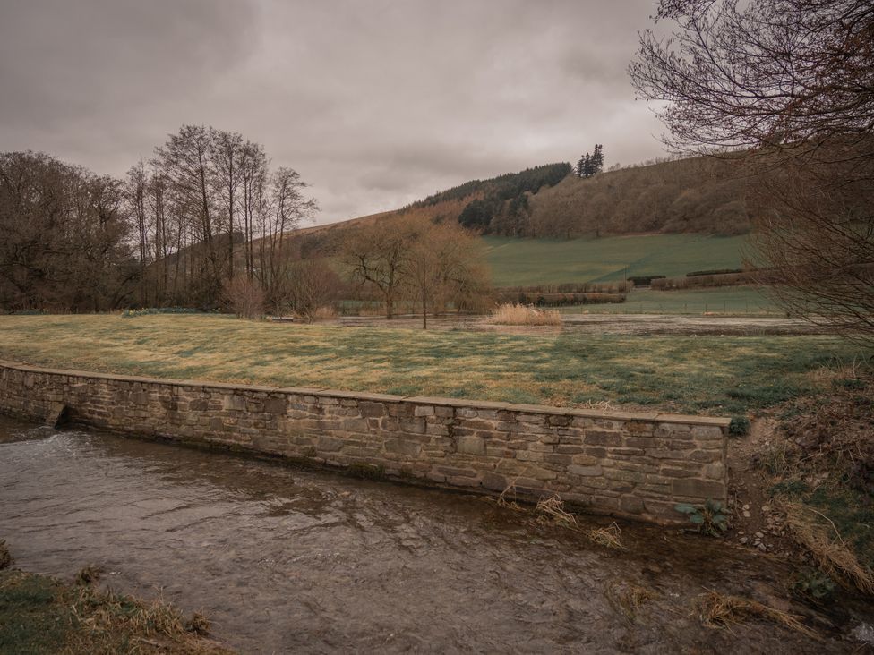 A stream next to a stone wall and grass with trees and hills in the background at Stud Farm House Bleddfa near Knighton