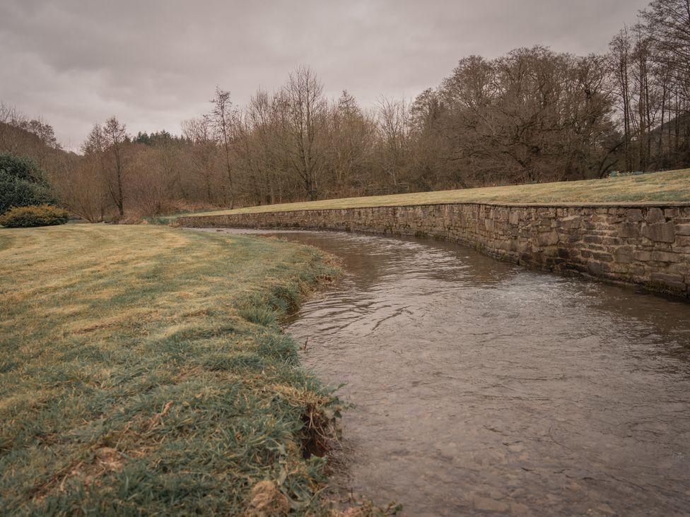 A river flowing alongside a stone wall and grassy area at Stud Farm House in Bleddfa near Knighton