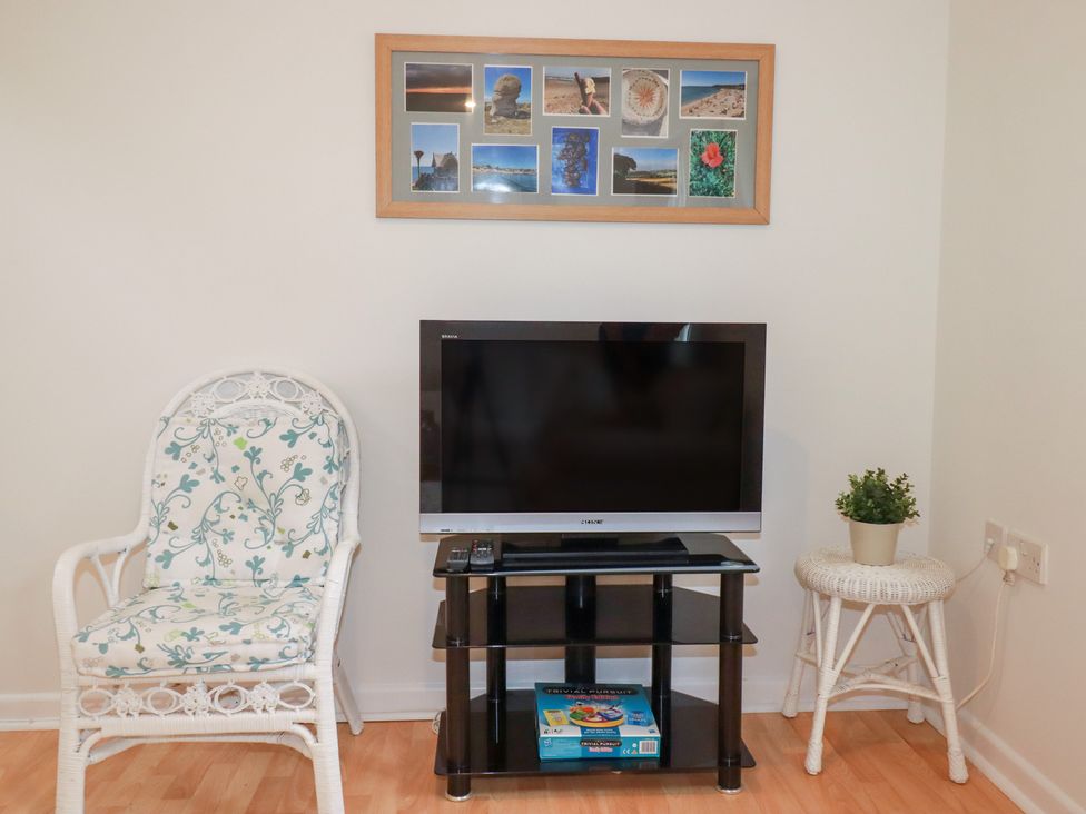 A living room with a TV on a stand and a chair at Acorns in Falmouth