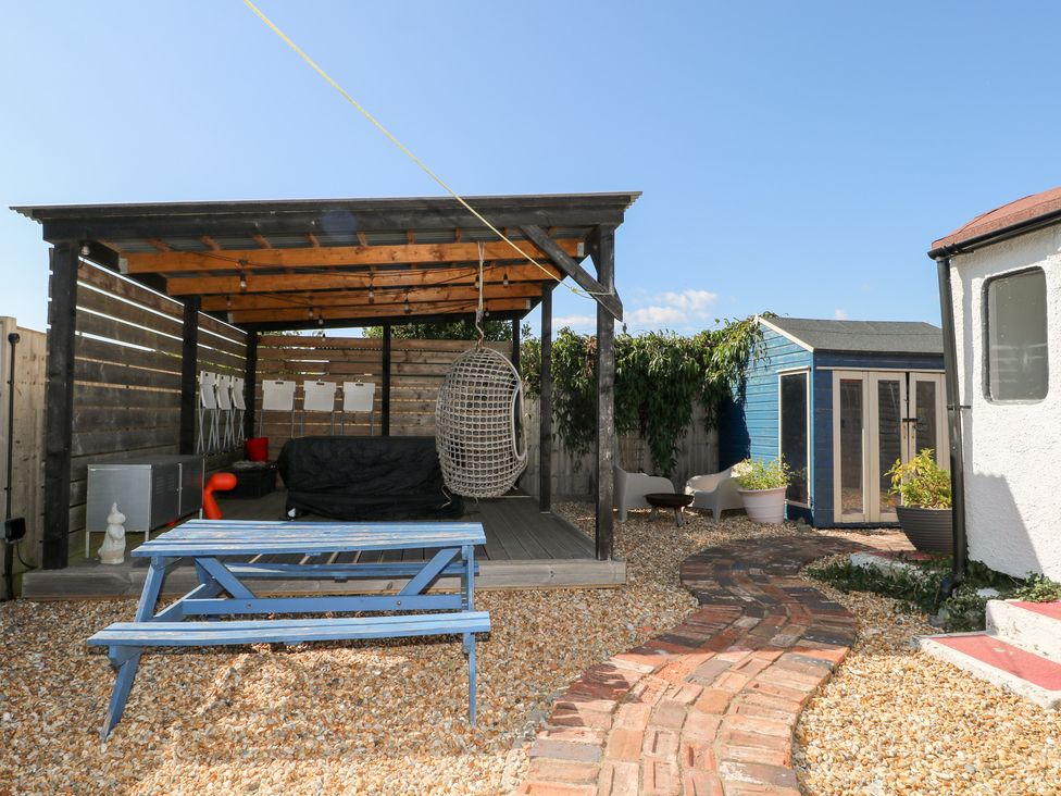 An outdoor shelter with a hanging chair and table in the garden at Harbour Road Quirky Beach Railway Carriages Pagham