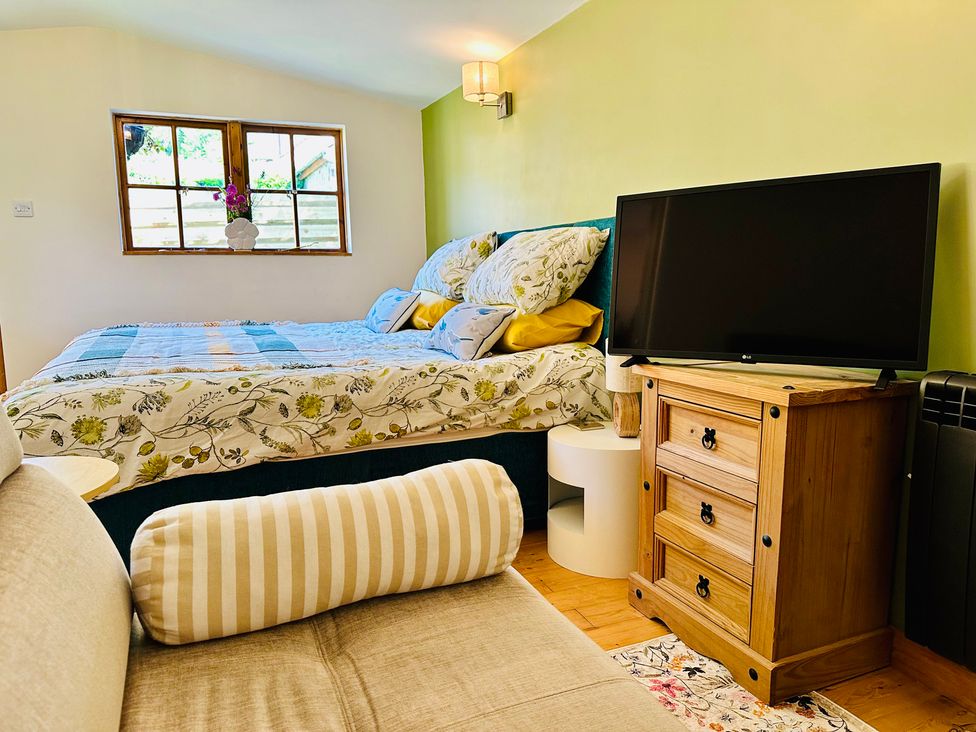 A bedroom with a bed, television, and nightstand at Harvey's Lodge in Helston