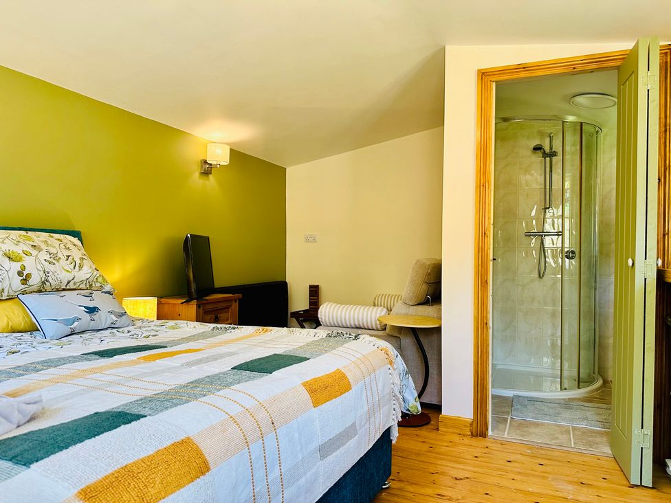 A bedroom with a bed, TV, armchair and shower at Harvey's Lodge in Helston