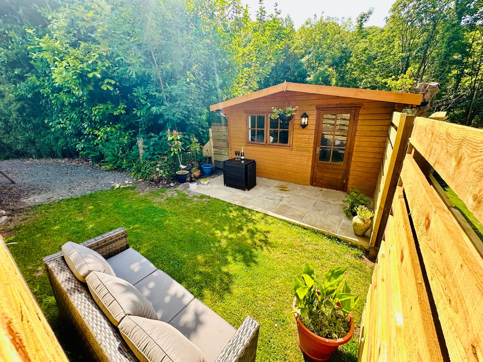 A garden with a log cabin and sofa at Harvey's Lodge in Helston