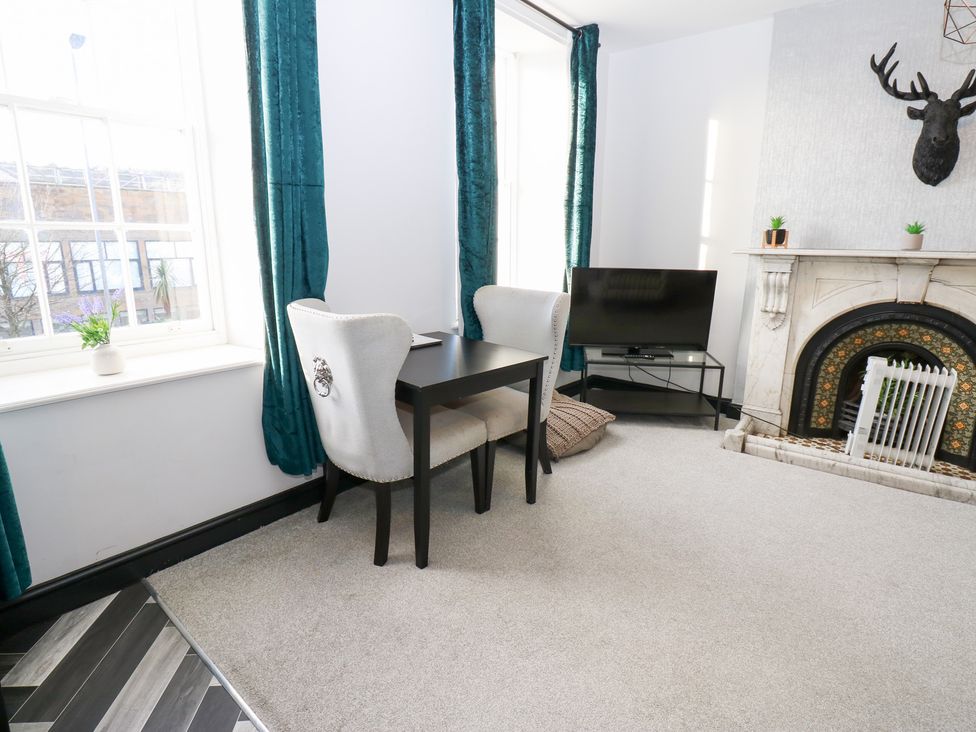A living room with a table and chair beside a fireplace at Lowther Apartment in Whitehaven