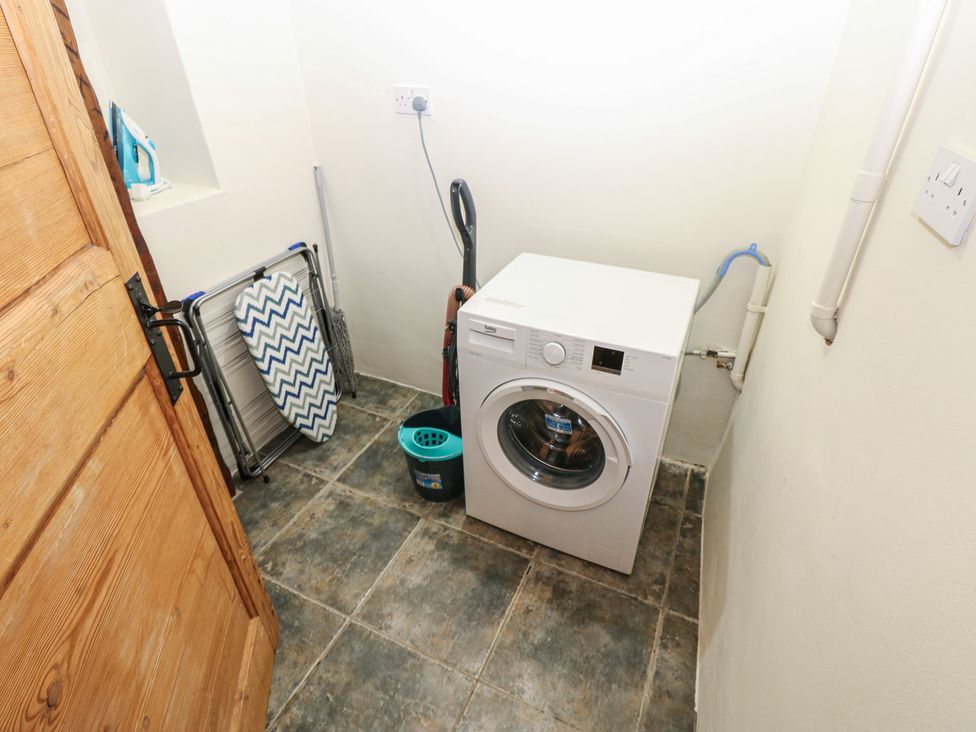 A laundry room with a washing machine and ironing board at Kirkgate Cottage in Cockermouth