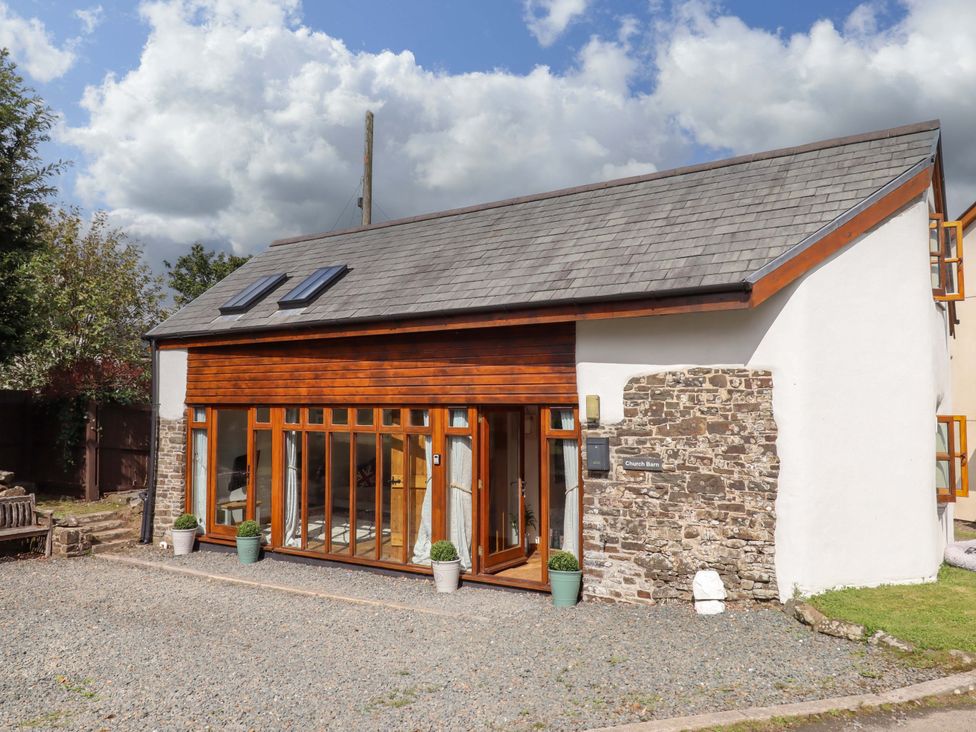 An exterior view of a building with large windows and stone wall at Church Barn Sutcombe near Bradworthy