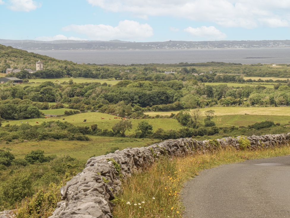 A landscape with a stone wall and fields near a water body at Kate's Cottage