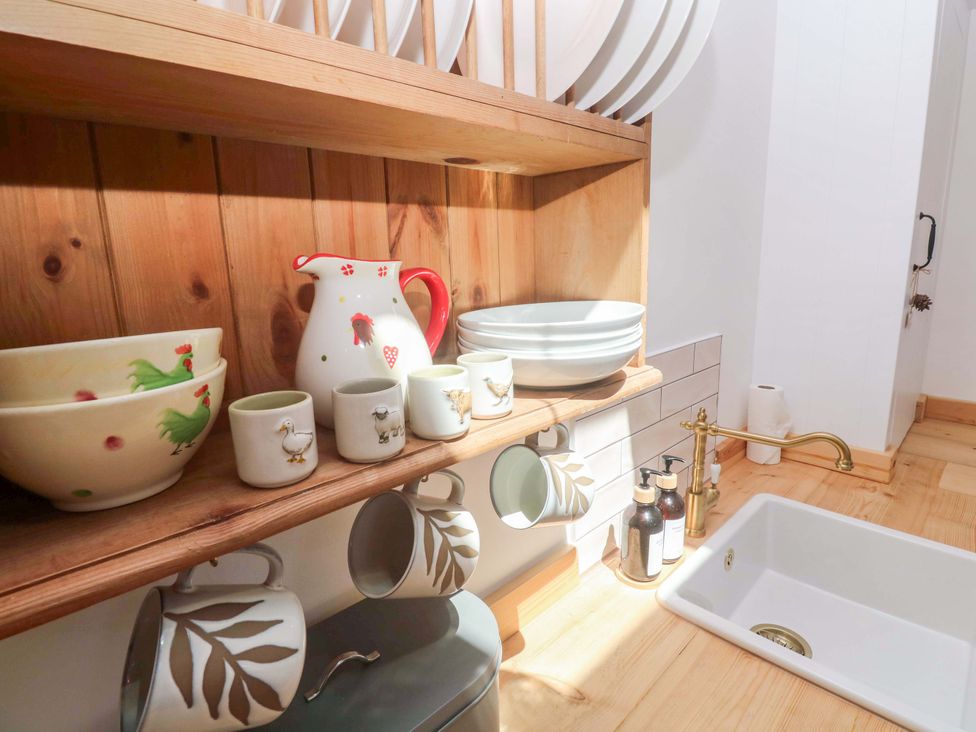A kitchen with dishes on a shelf and a sink at Lavender Cottage