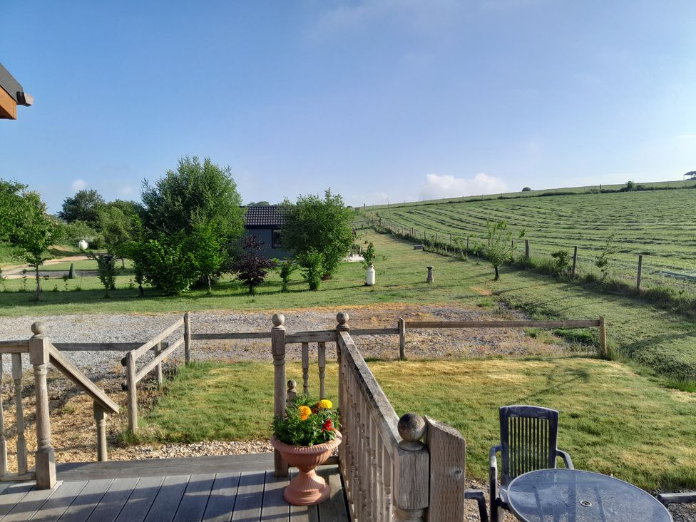 A wooden deck with a flower pot and furniture overlooking a grassy field at The Buckland Pentridge near Sixpenny Handley