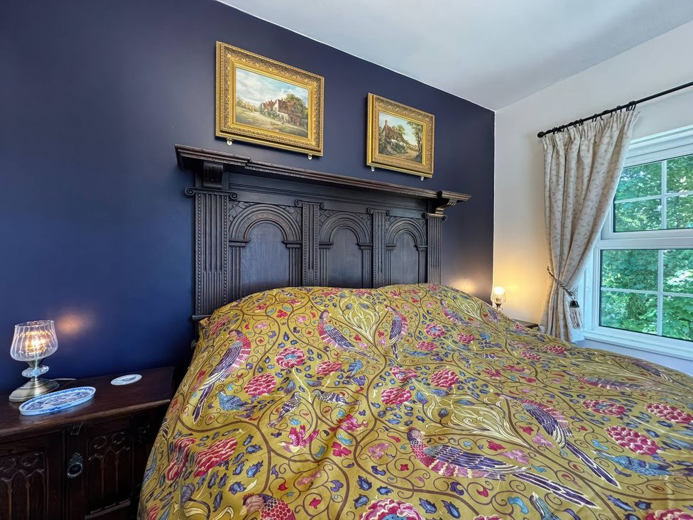A bedroom with a bed, nightstand, lamp, and pictures at St. James Cottage, Liskeard