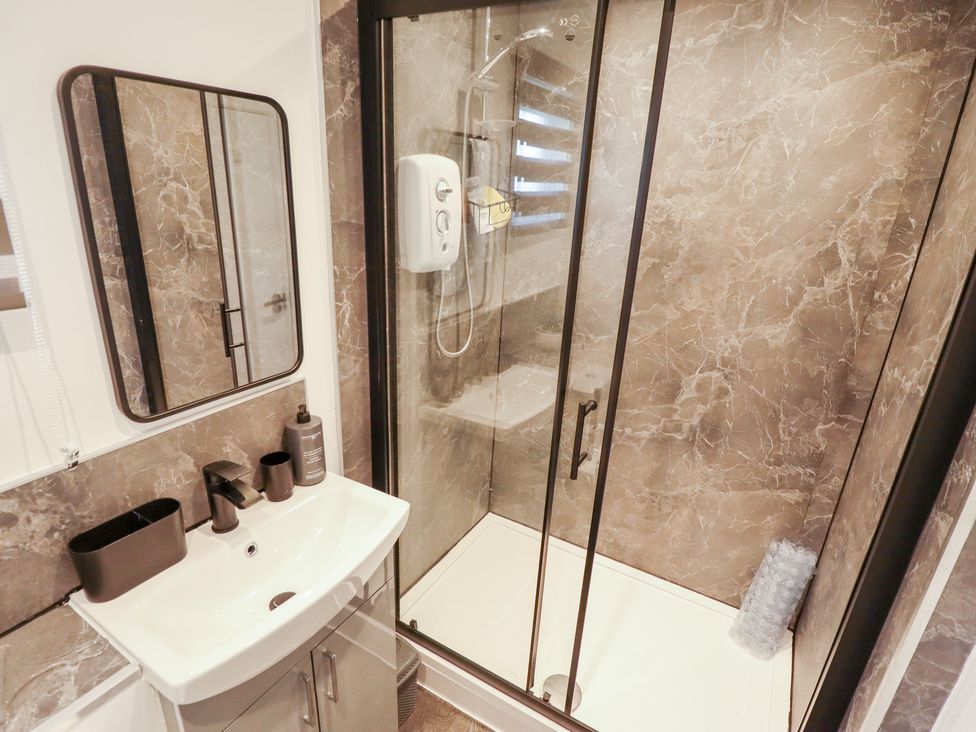 A bathroom with a shower, sink, and mirror at 66 Cherry Park Skegness