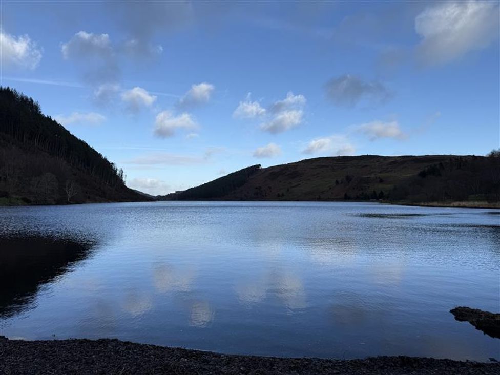 A lake surrounded by hills and trees at Ty Newydd in Llanrhychwyn near Llanrwst