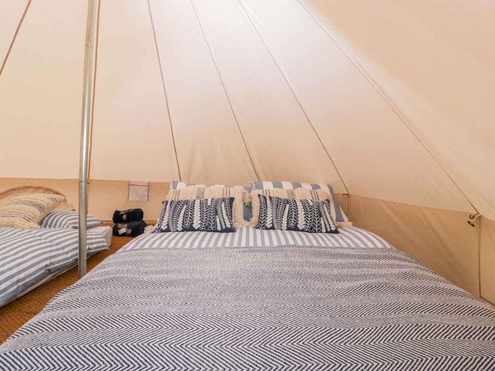 A tent interior with a bed and decorated pillows at Bell 2, Shades Farm near Malmesbury