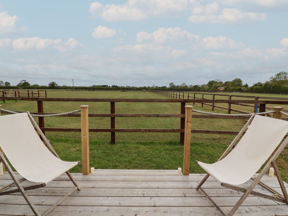 A deck with chairs overlooking a fenced lawn at Bell 2 Shades Farm near Minety