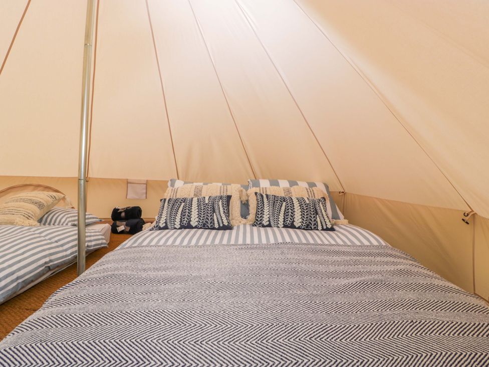 A tent interior with a bed and cushions at Bell 3 Shades Farm near Malmesbury