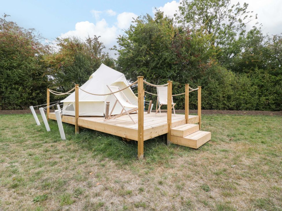A tent on a wooden deck with chairs and steps at Bell 3 Shades Farm near Malmesbury