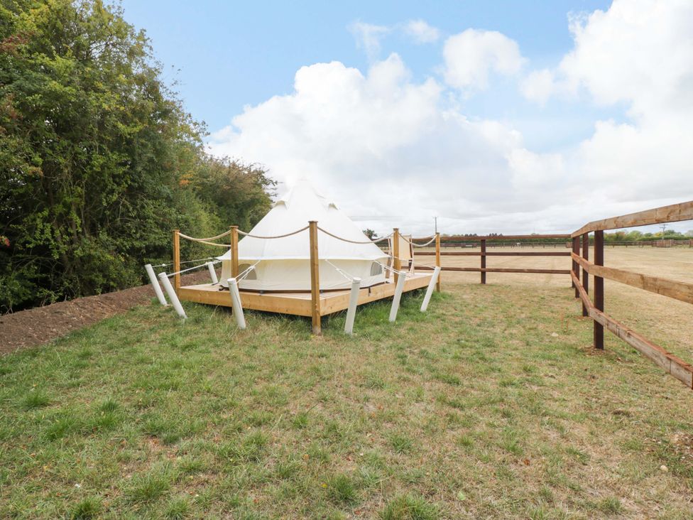 A tent on a wooden deck with grass around at Bell 3 near Shades Farm Mallmesbury
