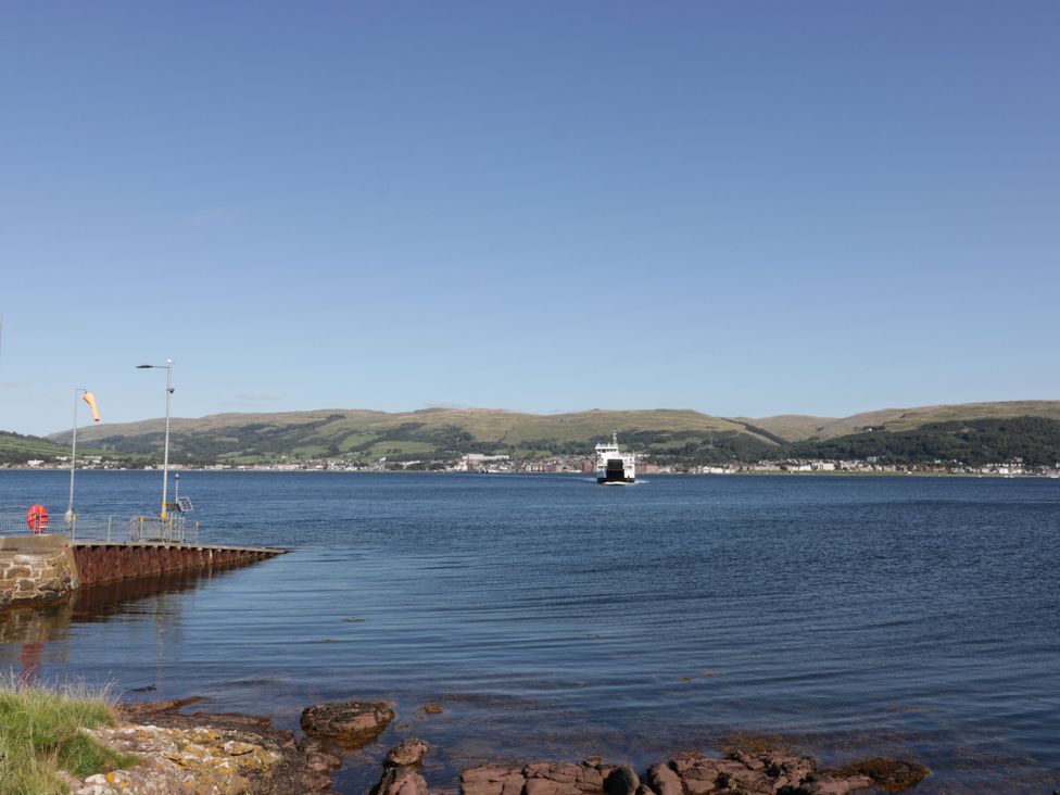 A view of a ferry on water with a pier and hills in the background at 6 George Street Isle of Cumbrae