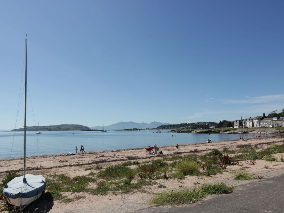 A beach with people and a sailboat at 6 George Street Isle of Cumbrae